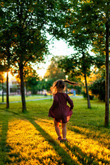 Wall Mural - happy child girl on a walk in the park near the house at sunset, summer time