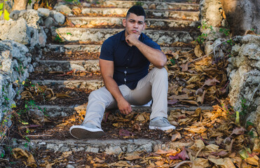 White-skinned male model of Venezuelan origin in the Dominican Republic. sexy man in jeans in the park outdoors with orange walks with natural sunlight among the leaves sitting on the stairs