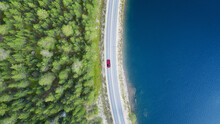 Aerial View Of Mountain Curve Road With Red Car. Aerial View Of Road Between Green  Forest And Blue Lake. Top View From Flying Drone.