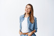 © Cookie Studio - Happy carefree woman with joyful expression, smiling while standing in relaxed pose against white background, holding hands in jeans pockets