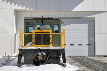 Railway maintenance vehicle parked on tracks in snow in front of a large garage nobody