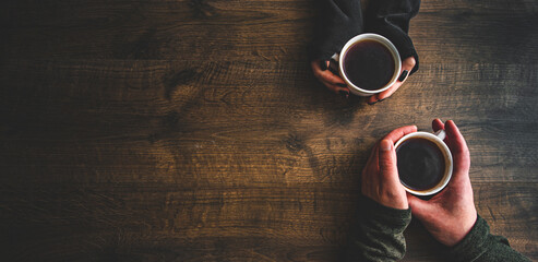 Cups of black tea or coffee in the hands of men and women. on a wooden background. with copy space. top view