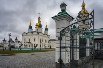 View of the Tobolsk Kremlin on a cloudy autumn day. Ancient churches with gold and blue domes, cast lattices with ornate patterns, historic buildings of white stone, towers with triangular roofs 