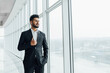 Indian man in black suit by the window in a modern building, businessman in the office