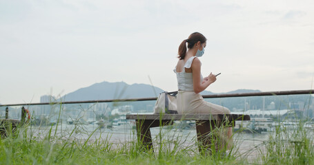 Wall Mural - Woman wear face mask and use of mobile phone at park