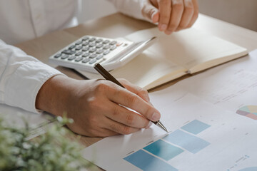 Close up hand of young asian businessman ,male is analyzing charts, reports on paperwork, document to calculate the cost, budget of business .Finance, financial analysis of growth concept.