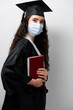 © Rabizo Anatolii - Student with book in graduation robe and cap in medical mask at coronavirus covid-19 period. Future leader of science. Academician young woman in black gown smiling.
