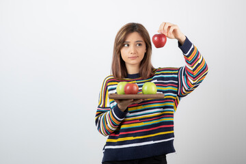 Wall Mural - Adorable young girl in casual clothes showing red apples over white wall