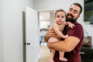 Man with beard holding cubby naked baby boy in bedroom 