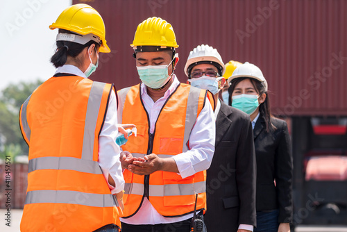 Factory workers wear face mask and safety dress cleaning hand with alcohol sanitizer gel and stand on queue at outdoor warehouse - safety and health  protect coronavirus protocol concept