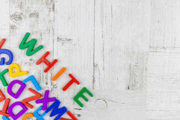 Fototapete - Brightly colored alphabet letters spelling word - White - arranged diagonally above a corner decoration of random colorful letters on a white wood background with copyspace. Flat lay, top view