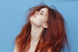 red-haired woman with tangled hair on her head on blue background cropped view