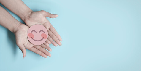 Wall Mural - Hand holding blue paper cut happy smile face, positive thinking, mental health assessment , world mental health day concept	