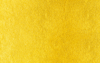 Gold wall texture background. Yellow shiny gold foil paint on wall surface with light reflection, vibrant golden luxury wallpaper