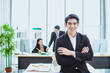 © anusak - young asian business man. smile face. sitting and standing in office. talk business. phone call with official working background. looking camera cross arm copy space