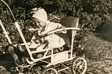 Wall Mural - Latvia - CIRCA 1940s: Portrait of baby girl sitting in carriage. Baby stroller pram. Vintage archive Art Deco era photography