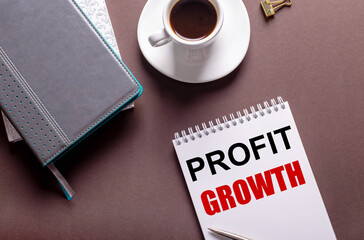 Fototapete - On a brown background, diaries, a white cup of coffee and a notebook with inscription PROFIT GROWTH