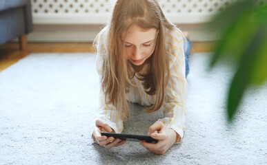 Wall Mural - Tween girl with smartphone lying on the carpet.