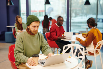 Wall Mural - Serious bearded businesswoman with glass of coffee looking at laptop display