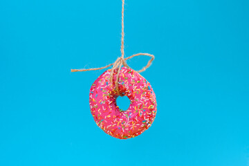 A round doughnut with pink frosting, suspended on a string. Close-up. Blue background. Copy space