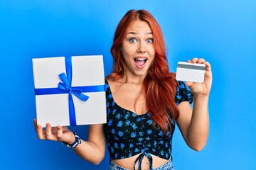 Sticker - Young redhead woman holding gift and credit card celebrating crazy and amazed for success with open eyes screaming excited.