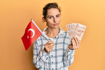 Sticker - Young brunette woman holding turkey flag and liras banknotes relaxed with serious expression on face. simple and natural looking at the camera.