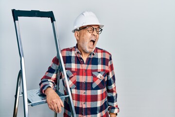 Sticker - Handsome mature handyman close to construction stairs wearing hardhat angry and mad screaming frustrated and furious, shouting with anger. rage and aggressive concept.