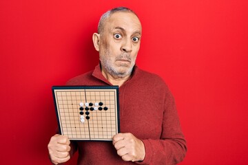 Sticker - Handsome mature man holding asian go game board clueless and confused expression. doubt concept.