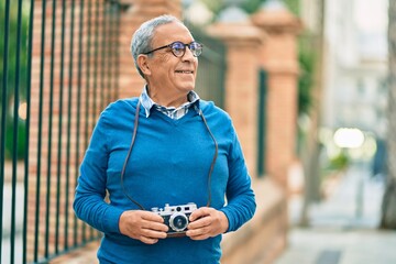 Wall Mural - senior grey-haired tourist man smiling happy using vintage camera at the city.