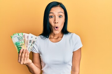 Sticker - Beautiful hispanic woman holding russian ruble banknotes scared and amazed with open mouth for surprise, disbelief face