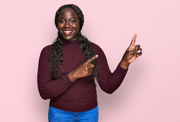 Sticker - Young african woman wearing casual winter sweater smiling and looking at the camera pointing with two hands and fingers to the side.