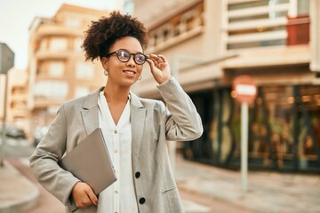 Canvas Print - Young african american businesswoman smiling happy holding laptop at the city.