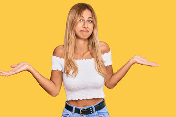 Poster - Beautiful blonde young woman wearing casual white tshirt clueless and confused expression with arms and hands raised. doubt concept.