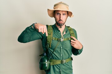 Wall Mural - Handsome man with beard wearing explorer hat and backpack pointing down looking sad and upset, indicating direction with fingers, unhappy and depressed.