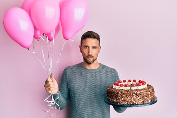 Sticker - Handsome man with beard celebrating birthday with cake holding balloons relaxed with serious expression on face. simple and natural looking at the camera.