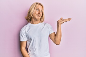 Poster - Caucasian young man with long hair wearing casual white t shirt smiling cheerful presenting and pointing with palm of hand looking at the camera.