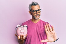 Middle Age Grey-haired Man Holding Piggy Bank With Glasses With Open Hand Doing Stop Sign With Serious And Confident Expression, Defense Gesture