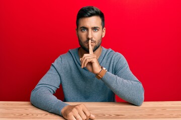 Wall Mural - Handsome hispanic man wearing casual style sitting on the table asking to be quiet with finger on lips. silence and secret concept.