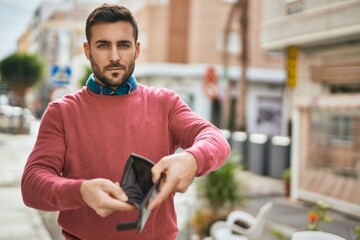 Young hispanic man with serious expression showing empty wallet at the city.