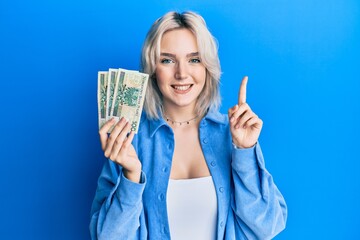 Sticker - Young blonde girl holding 50 polish zloty banknotes smiling with an idea or question pointing finger with happy face, number one