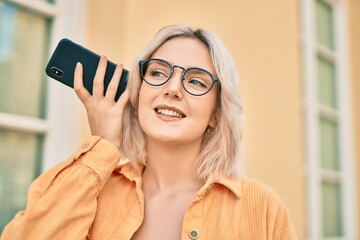 Sticker - Young blonde girl smiling happy listening audio message using smartphone at the city.