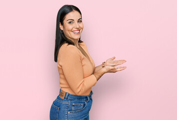 Young hispanic woman wearing casual clothes pointing aside with hands open palms showing copy space, presenting advertisement smiling excited happy