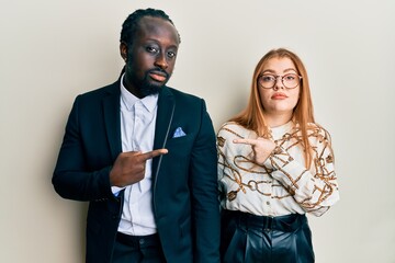 Sticker - Young interracial couple wearing business and elegant clothes pointing with hand finger to the side showing advertisement, serious and calm face