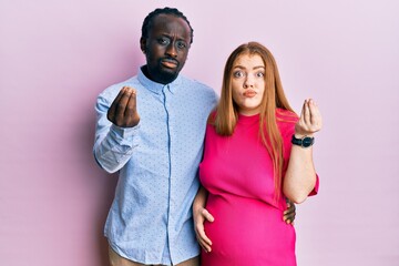 Sticker - Young interracial couple expecting a baby, touching pregnant belly doing italian gesture with hand and fingers confident expression