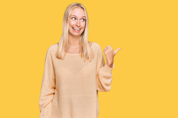 Canvas Print - Young blonde girl wearing casual clothes smiling with happy face looking and pointing to the side with thumb up.