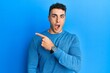 © Krakenimages.com - Hispanic young man wearing casual winter sweater surprised pointing with finger to the side, open mouth amazed expression.