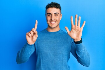 Hispanic young man wearing casual winter sweater showing and pointing up with fingers number six while smiling confident and happy.