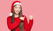 Young Chinese Woman Wearing Christmas Hat Pointing To The Back Behind With Hand And Thumbs Up, Smiling Confident