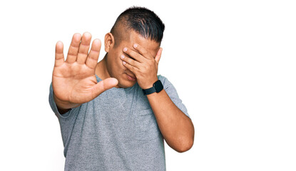 Young latin man wearing casual clothes covering eyes with hands and doing stop gesture with sad and fear expression. embarrassed and negative concept.