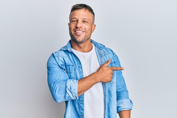 Wall Mural - Handsome muscle man wearing casual denim jacket cheerful with a smile of face pointing with hand and finger up to the side with happy and natural expression on face